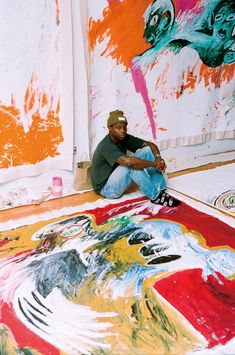 a man sitting on the ground in front of paintings