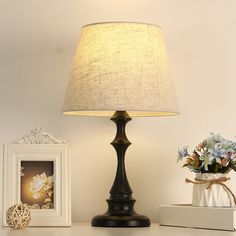 a lamp sitting on top of a table next to a vase with flowers in it