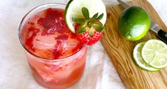 a strawberry margarita with limes and strawberries on a cutting board next to a knife