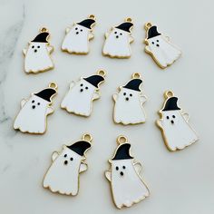 white ghost charms with black hat and eyes on a marble counter top, set in gold - plated setting