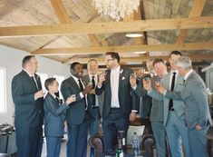 a group of men standing next to each other holding wine glasses in their hands while wearing suits