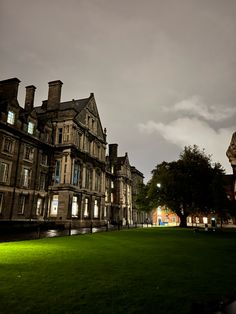 an old building is lit up at night with green grass in the foreground and dark clouds in the background