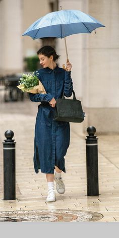 a woman walking down the street with an umbrella over her head and flowers in her hand