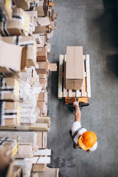 a man in an orange hard hat and safety vest standing next to pallets with boxes on them