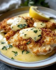 two pieces of chicken covered in sauce and parmesan cheese on a plate with lemon wedges