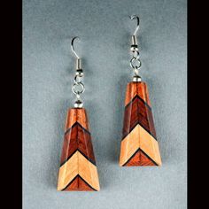 two pairs of wooden earrings with metal earwires on a gray background, one is made out of wood and the other has an arrow shaped design