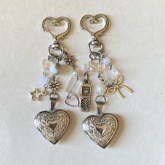 two silver heart shaped charms on a white surface with beads and charms attached to them