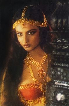 a woman with long black hair and gold jewelry on her head is looking at the camera