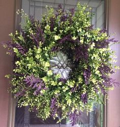 a wreath hanging on the front door of a house with purple flowers and green leaves