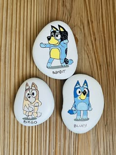 three rocks with cartoon characters painted on them sitting on a wooden surface, next to each other