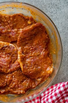 some meat is in a bowl on a table top with a red and white checkered napkin