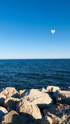 a heart - shaped balloon floats over the water from rocks in front of an ocean