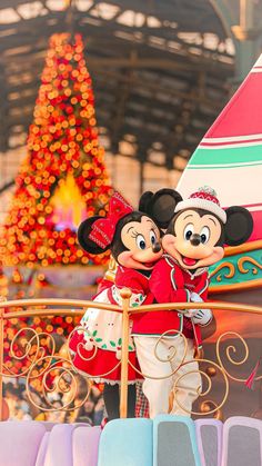 two mickey and minnie mouse characters in front of a christmas tree at the disneyland world