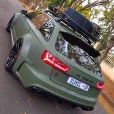 the rear end of a green car with luggage strapped to it's roof rack