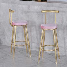 two gold barstools with pink cushions sit in front of a concrete countertop