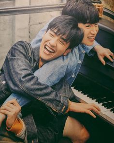 two young men hugging each other while sitting on top of an old piano in front of a brick wall