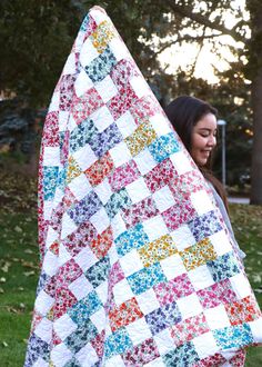 a woman holding up a quilt in the grass