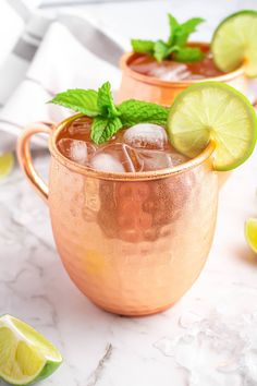 two copper mugs filled with ice, lime and mint garnish on a marble surface