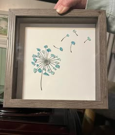 a person holding up a frame with a drawing of a dandelion