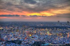 an aerial view of a city at sunset with clouds in the sky and buildings lit up