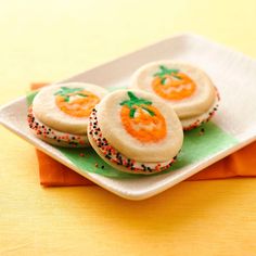 three cookies with sprinkles on a plate next to an orange napkin and fork