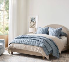 a bed with blue and white comforters in a bedroom next to a chair, ottoman and window