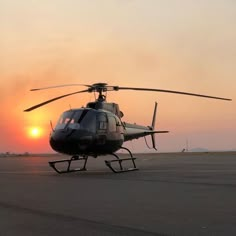 a helicopter sitting on top of an airport tarmac with the sun setting in the background