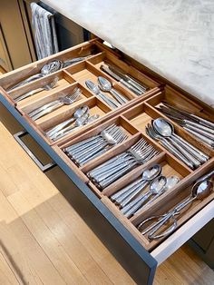 an open drawer with silverware in it sitting on a wooden floor next to a counter