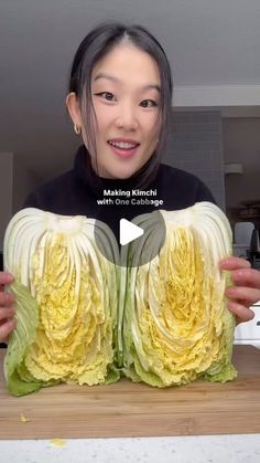 a woman holding up two large cabbages on top of a wooden cutting board with the words making kimchi with one cabbage