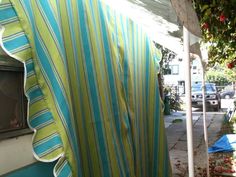 a blue and green striped curtain hanging from a white awning next to a tree