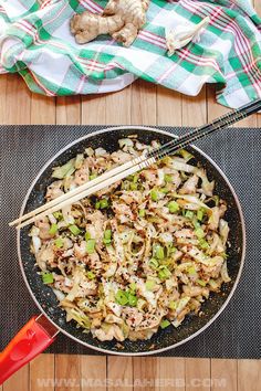 a wok filled with stir fried vegetables and chopsticks on top of a wooden table