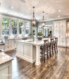 a large kitchen with white cabinets and wood flooring, along with an island in the middle