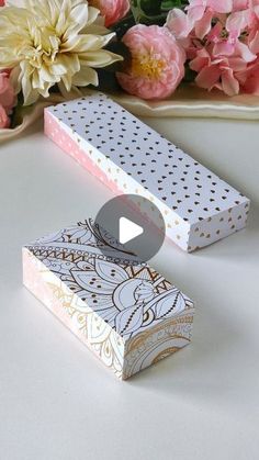 two decorative boxes sitting on top of a table next to pink flowers and a plate