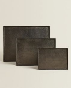 three square metal trays in various sizes and colors, one with a black leather finish