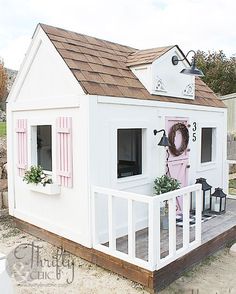 a small white house with pink shutters on the front and side windows, sitting next to a fence