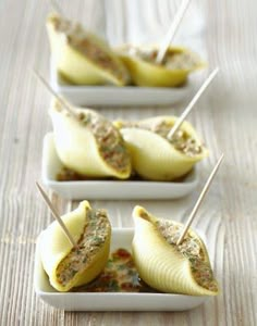 three small white dishes filled with food on top of a wooden table and toothpicks sticking out of them