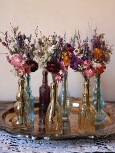 four glass vases with flowers in them on a tray