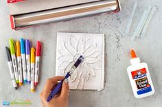 a person is painting on paper with markers and paintbrushes next to some crafting supplies