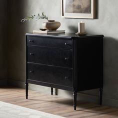 a black dresser in a room with a painting on the wall and a candle next to it