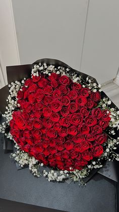 a large bouquet of red roses in the shape of a heart on top of a black box