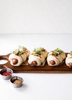 five hot dogs wrapped in buns and topped with toppings on a wooden platter