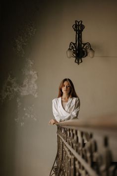 a woman leaning on a railing in front of a wall with a chandelier