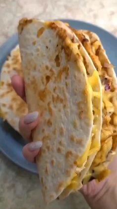 a person holding up a tortilla with cheese on it in front of a plate