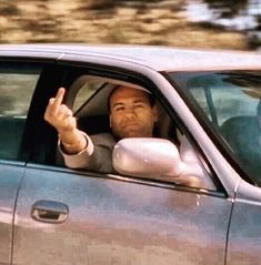 a man sitting in the driver's seat of a car holding his hand up