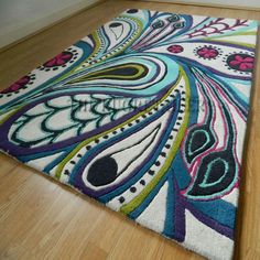 the rug is on the wooden floor and it looks like an artistic design with colorful feathers