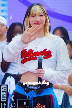 a girl with blonde hair is holding a microphone and wearing a white cropped shirt