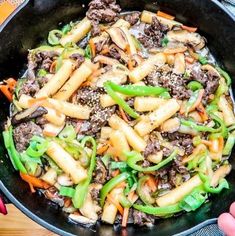 a skillet filled with pasta and vegetables on top of a wooden table