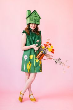 a woman in a green dress holding flowers and a house on top of her head