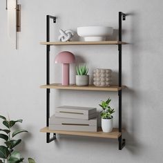 three shelves with plants, books and other items on them next to a wall lamp