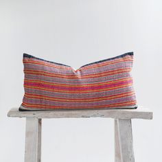 a colorful striped pillow sitting on top of a wooden bench next to a white wall